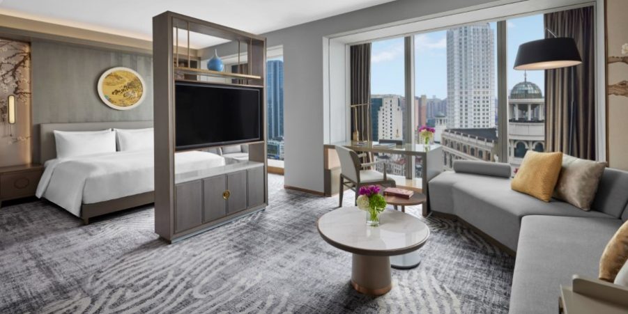 Interior of a hotel room with a spacious bed, a cozy couch, and a mounted television on the wall.